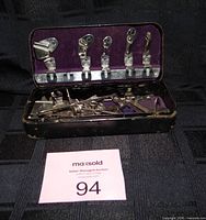 Open tin showing six presser feet clipped to lid and loose attachments in base