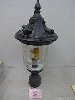 Full view of lantern showing matte black body, glass shade, bulb, and post base
