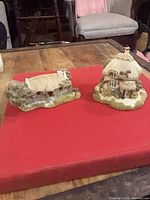 Both Lilliput Lane cottage figurines on red surface