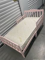 Full view of pink toddler bed frame with mattress in place