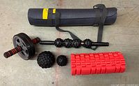 All items laid out: yoga mat, foam roller, ab wheel, massage stick, two massage balls