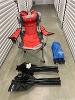 Red-grey padded camp chair opened beside folded chairs and cot bag