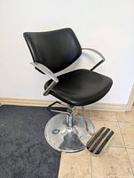 Front view of black vinyl salon chair showing seat, backrest, chrome armrests and hydraulic base
