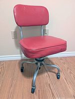 Front left view of red vinyl swivel chair showing seat, backrest, metal frame and casters