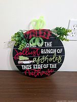 Front view of round sign showing text, greenery, bow and hanger