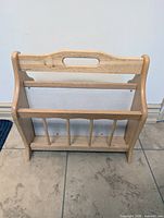 Front view of wooden magazine rack showing handle cutout, dowel bars, white back panel