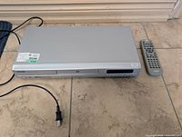 Front angled view of Toshiba DVD player with remote and power cord