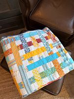 Quilt folded on ottoman showing patchwork colors and stitching