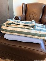 Both folded duvet covers stacked on leather ottoman; stripe pattern visible on top, blue cover beneath