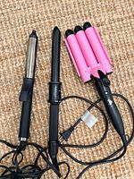 Three styling tools laid out: curling iron, wand, triple waver