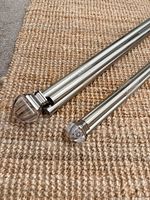 Close view of both rods showing brushed metal finish and clear finials