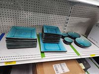 Shelf view showing stacks of turquoise square plates and matching bowls