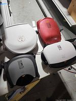 Four George Foreman grills in various colors on table
