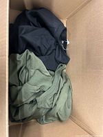 Overview of black garment and olive knit sweater inside box