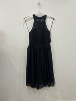 Full view of black lace cocktail dress on hanger