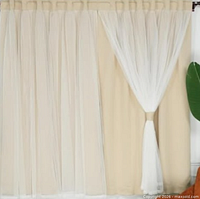 Installed view of beige blackout curtains with sheer overlay tied back