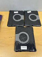 Three sealed black iPad cases with grey rotating kickstand shown front view
