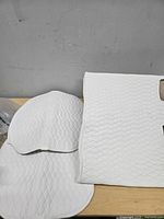 Two quilted white seat cover pieces on table