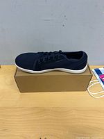 Side view of sneaker on box showing navy upper and white sole