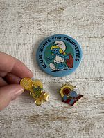 Front of three Smurf pins including large button and two enamel pins