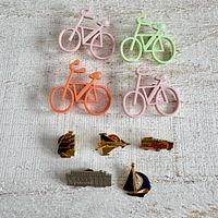 Overview showing five bicycle brooches in varying colours and six travel-themed enamel pins beneath