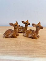 Three flocked plastic deer figurines seated on wood surface, frontal angle