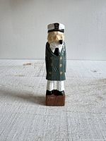 Front view of hand-carved wood sailor figurine showing face, coat and hat