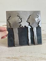 Front view of square steel tile showing three raised tree silhouettes