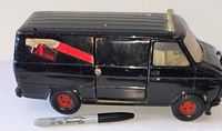 Left side view of black diecast A-Team van with red wheels and torn side decal, marker for scale