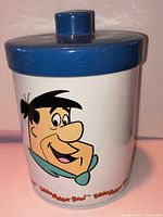 Front view of cylindrical cookie jar showing Fred Flintstone decal and blue lid