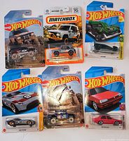 All six sealed Hot Wheels and Matchbox cars displayed front of cards