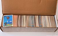 open cardboard storage box filled with upright baseball cards; one card pulled forward for example