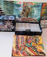 Overall view of open Legendary Dragon Decks box filled with cards, backdrop showing large winged creature artwork, playmat visible foreground