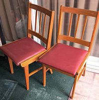Two matching wooden chairs with red vinyl seats displayed side by side