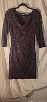 Full front view of deep plum sequined lace sheath dress on hanger