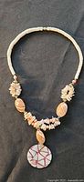 Full necklace view showing heishi shell strand, shell chip clusters, oval shells and mosaic pendant