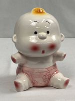Front view of ceramic baby coin bank showing facial features and pink diaper