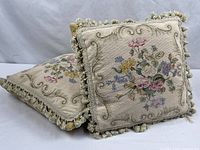 Two needlepoint pillows showing floral fronts and tassel trim