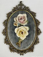 Front view of oval wall decor showing porcelain roses on blue velvet in ornate metal frame