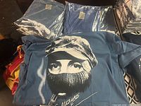 Light blue Che Guevara T-shirt with portrait graphic, packaged shirts behind