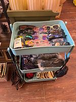 Blue rolling cart top tray filled with assorted sunglasses; fanny packs and pouches hanging on sides