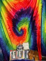 Rainbow tie-dye tapestry draped as backdrop with disco ball, wrapped curtain, paperwork, sandals visible