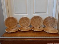 Eight wicker chargers lined upright and flat on wooden surface with ruler for scale