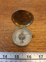 Open brass pocket compass showing dial and needle with ruler for scale