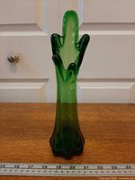Front view of green glass swung vase with ruler for scale