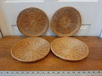 Four wicker chargers on wood surface with ruler for scale