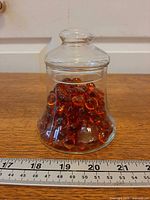 Jar filled with amber glass pebbles beside ruler