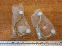 Two sealed gold-finish metal wall hooks with white ceramic knobs beside ruler for scale