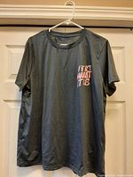 Front view of dark grey T-shirt on hanger showing overall design