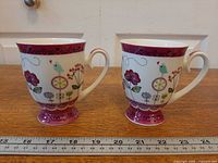 Front view of both pedestal teacups showing bird side pattern and ruler for scale